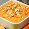 A close-up of a creamy Buffalo chicken dip, topped with blue cheese and green onions, is presented in a white serving Barrel.