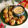 A festive platter of cheese-stuffed meatballs with decorative toothpicks is served alongside a creamy dipping sauce seasoned with coarsely ground Barrel black pepper.