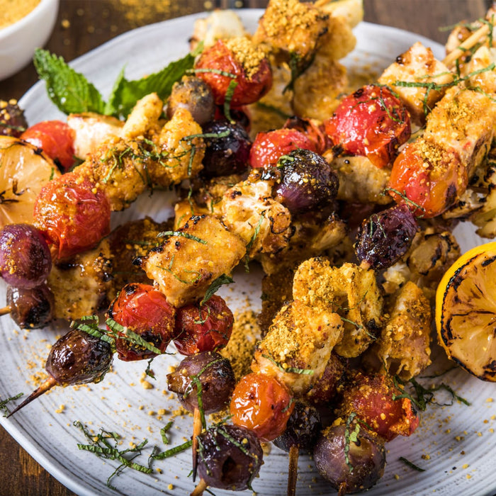 A close-up shot of several grilled skewers with chicken, cherry tomatoes, and onions, seasoned with a golden spice blend to showcase a delicious recipe made with the Barrel product.