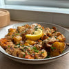 A white bowl filled with golden-brown smashed potatoes, garnished with grated cheese, chopped chives, and a lemon wedge.