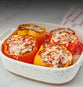 Baked stuffed bell peppers topped with melted cheese in a white speckled baking dish.