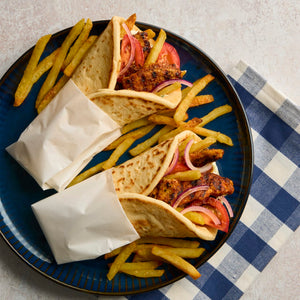 Two chicken gyros with french fries are served on a dark blue Barrel plate next to a checkered napkin.