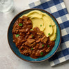A top-down view shows a hearty beef stew, perhaps made with a Barrel seasoning, served alongside creamy mashed potatoes in a rustic blue bowl.