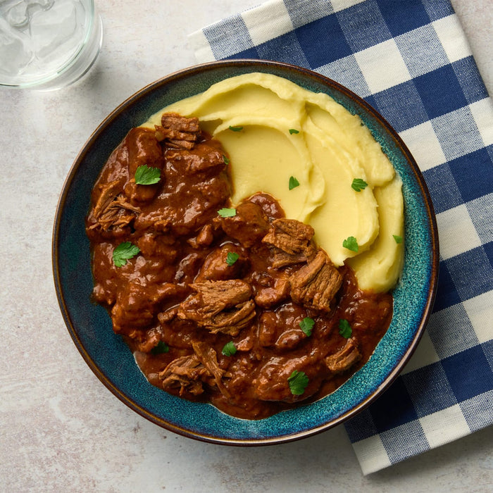 A top-down view shows a hearty beef stew, perhaps made with a Barrel seasoning, served alongside creamy mashed potatoes in a rustic blue bowl.
