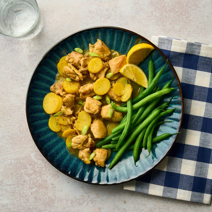 A delicious meal of chicken and potatoes with green beans is served on a rustic blue Barrel plate.
