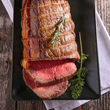 Roasted beef tenderloin on a black plate with herbs on a wooden surface