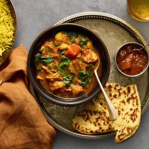 A bowl of chicken and spinach curry is served on a silver tray with naan bread, yellow rice, and chutney.