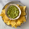 A bowl of fresh, chunky guacamole is centered on a rustic Barrel plate and surrounded by golden tortilla chips for dipping.