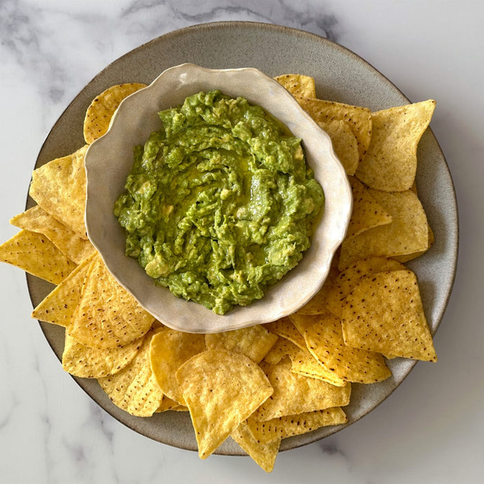 A bowl of fresh, chunky guacamole is centered on a rustic Barrel plate and surrounded by golden tortilla chips for dipping.
