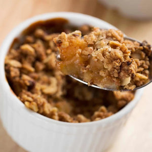 A spoonful of warm apple crumble, a perfect dessert to feature a Barrel spice blend, is lifted from a white ramekin.