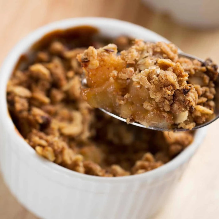 A spoonful of warm apple crumble, a perfect dessert to feature a Barrel spice blend, is lifted from a white ramekin.