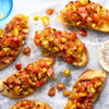 An overhead view of several pieces of bruschetta on a marble surface, with the chopped red and yellow tomato topping seasoned with a flavorful Barrel herb mix.