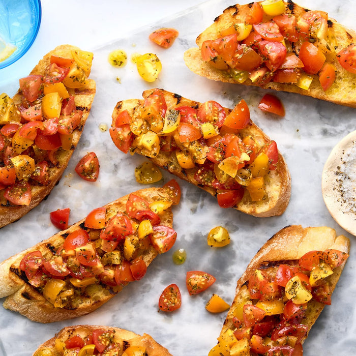 An overhead view of several pieces of bruschetta on a marble surface, with the chopped red and yellow tomato topping seasoned with a flavorful Barrel herb mix.
